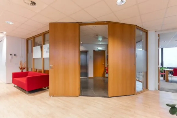 Ingang van een modern kantoor aan de 1e Hogeweg met houten deuren, rode zithoek en zicht op de lift.